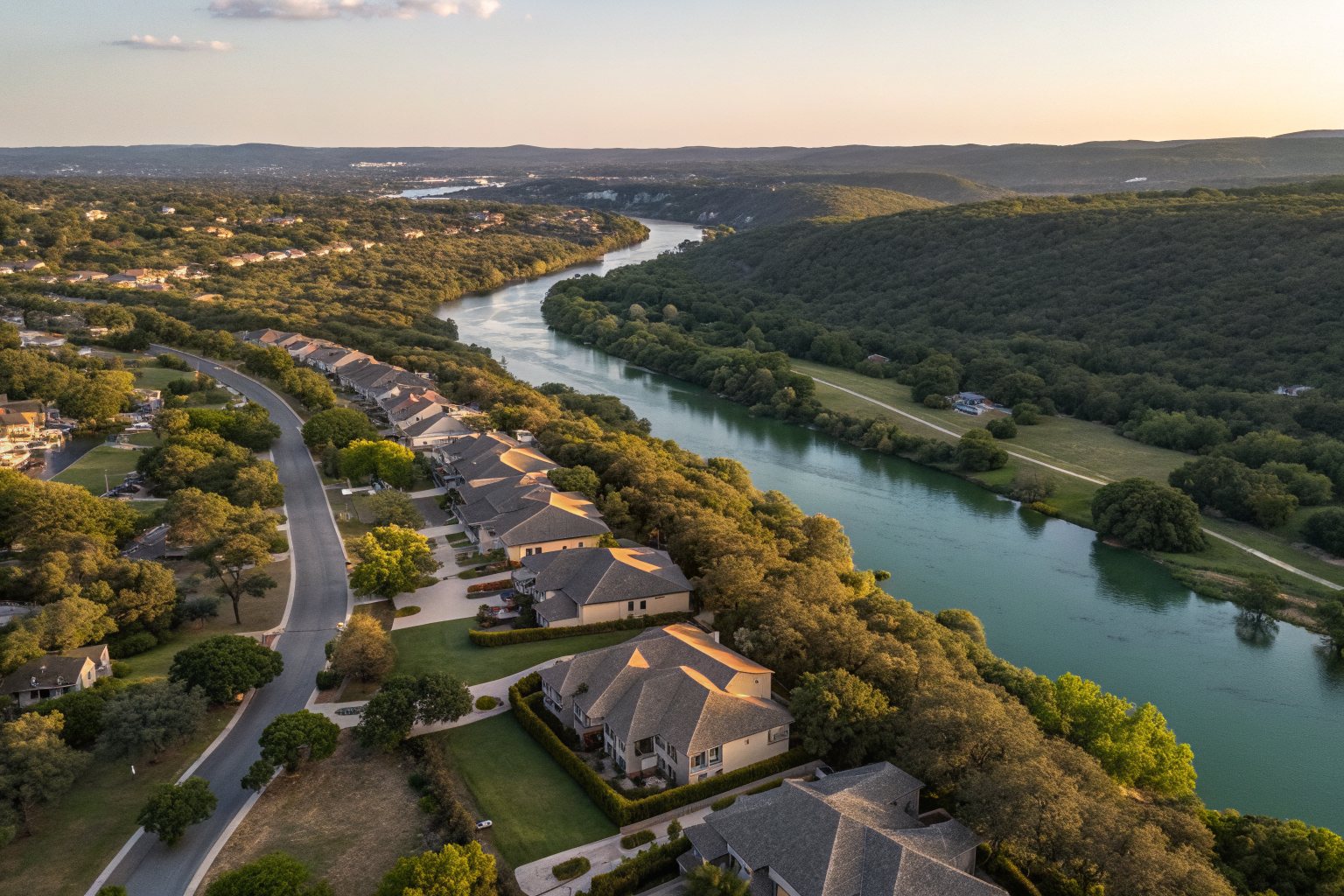 Aerial view of a hillside neighborhood of shingle-roofed homes beside a tree-lined green river